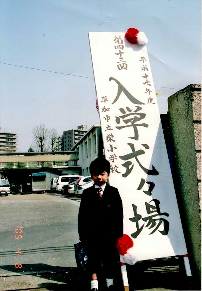 草加市立栄小学校の入学式看板の前に立つ幼少期の吉永一輝